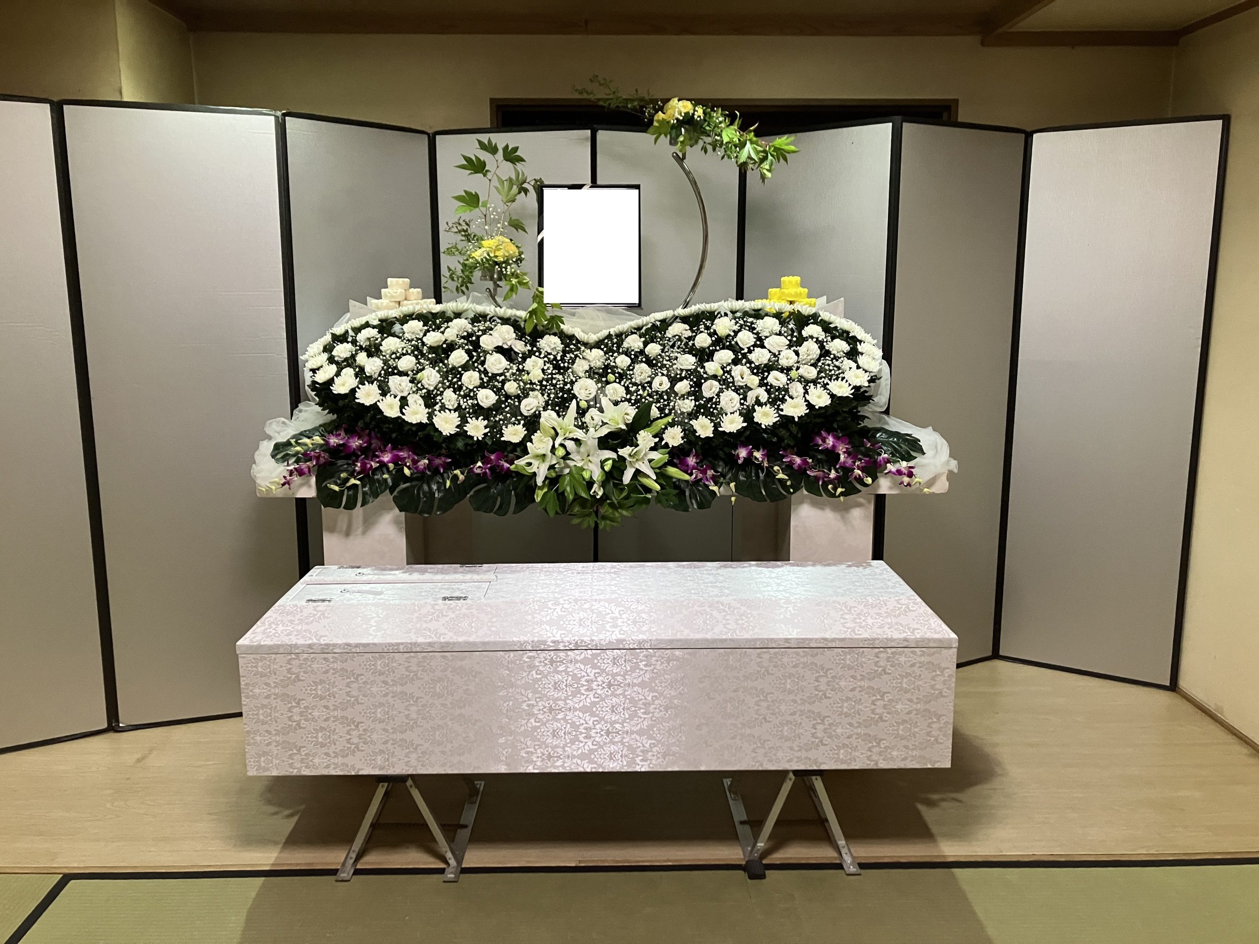 白い花と紫色の洋花を使用した生花祭壇と白い布張りのお棺